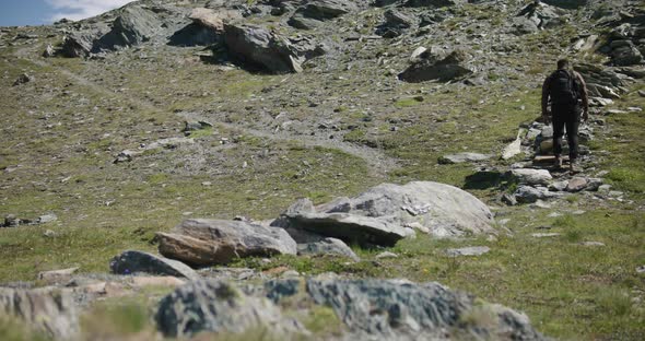 Black male traveler with backpack walking up hill exploring the Matterhorn mountainside in Switzerla alt