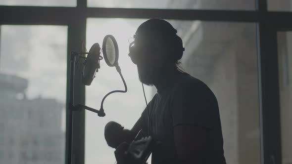 Young Man in Headphones Plays the Guitar and Sings Into the Studio Microphone