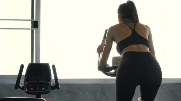 Rear View of Sporty Woman Riding Stationary Bike at the Gym alt