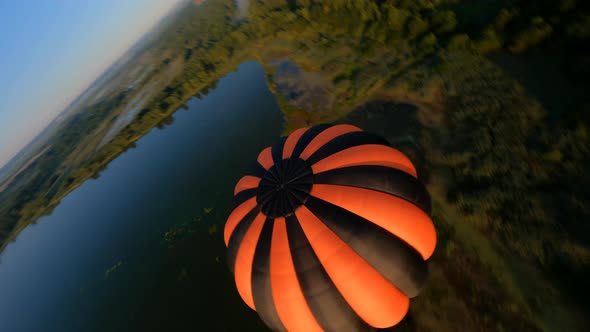 drone manoeuvres up and down around Black and orange hot air balloons above lake