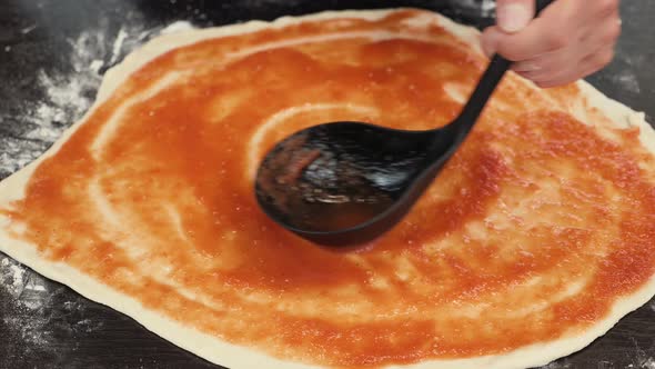 Female baker chef spreading tomato sauce on pizza dough, making pizza base alt