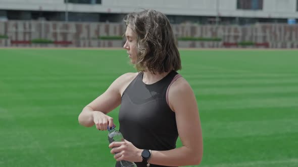 Sporty Brunette Enjoys Drinking Water After Hard Workout at Stadium alt