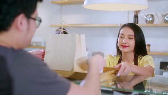 Attractive asian female cafe worker  giving takeaway food bag to customer alt