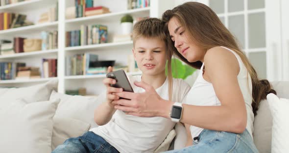 Young Mother and Son Looking at Smartphone Screen Browsing Internet Doing Shopping Online