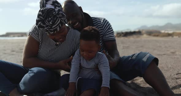African couple sitting on the beach and having playful time with little son alt