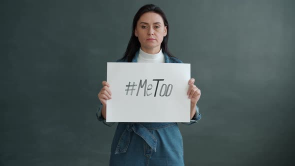 Slow Motion Portrait of Woman Holding MeToo Hashtag Banner and Looking at Camera Standing Alone alt