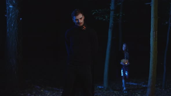 Wide Shot Scary Vampire Standing in Darkness in Forest As Little Brave Girl Walking From Trees alt