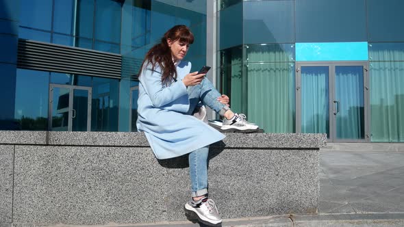 Pretty Girl in a Blue Coat with a Mobile Phone in Her Hands