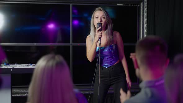 Portrait of Talented Beautiful Caucasian Blond Woman Singing with Microphone in Night Club with alt