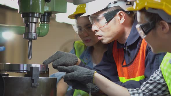 Asian male foreman showing case study of factory machine to two female trainee at construction site alt