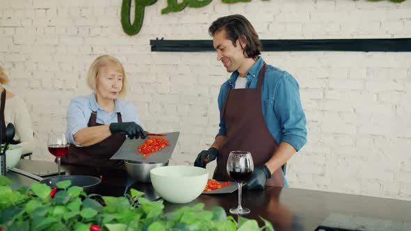 Women and Man in Aprons Cooking in Kitchen Talking During Culinary Master-class alt