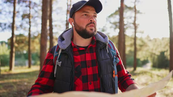 Traveler Stand in Forest and Look at Map in Hands and Looks for Way alt