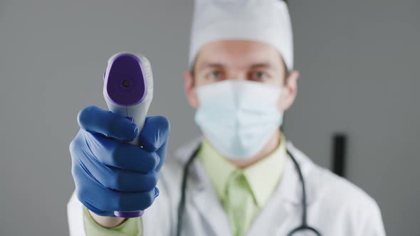 Healthcare Male Worker in a Medical Gown Doctor Holding and Testing Non Contact Infrared Thermometer alt