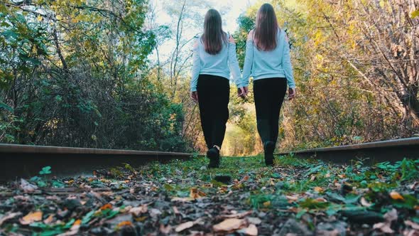 Twins Girls Holding Hands Walking Along Railroad Tracks alt