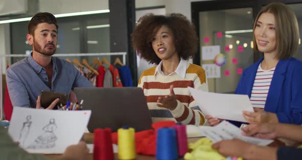 Mixed race colleagues sitting in office and discussing work over laptop alt