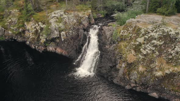 Panning from right to left of a waterfall falling towards a dark pool in the forest alt