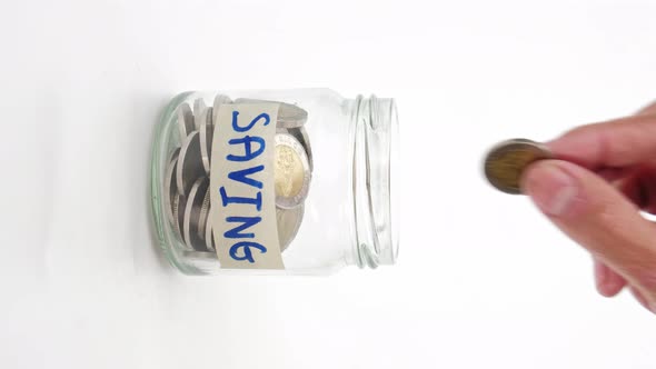 Hand is putting a coin or money in a glass jar on white background, Vertical video format.