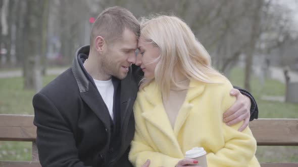 Loving Married Couple Rubbing Noses and Talking As Sitting on Bench in Park alt