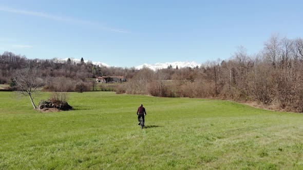Aerial: man having fun by riding mountain bike in the grass on sunny day, scenic alpine landscape alt