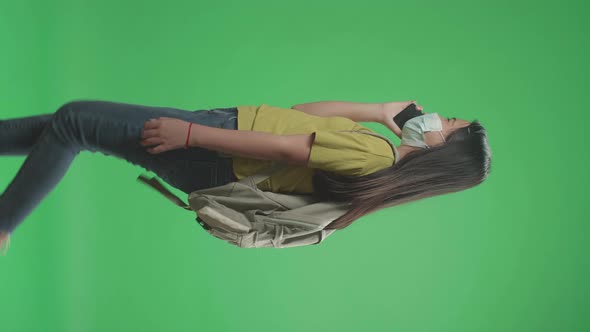Girl Student Wearing A Mask And Talking On Mobile Phone While Walking On Green Screen alt