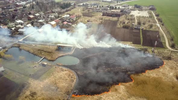 Aerial view of a field with dry grass set on fire with orange flames and high column of smoke. alt