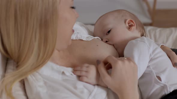 Young Blonde Woman Feeding with Breast and Stroking Her Baby Boy