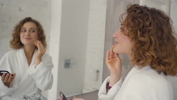 Beautiful Young Woman Applying Make-up Near Mirror in Bathroom alt