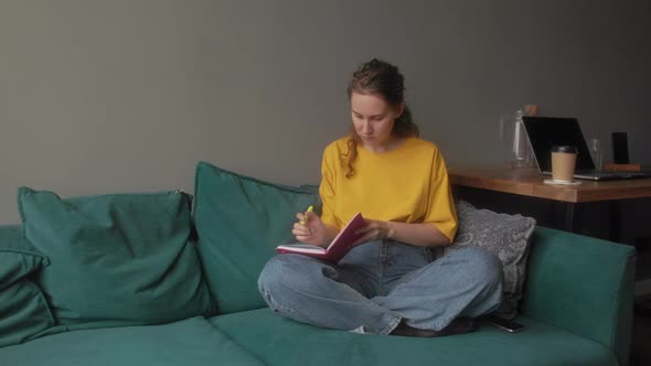 The Girl Makes Notes in a Notebook Sitting on a Bright Sofa