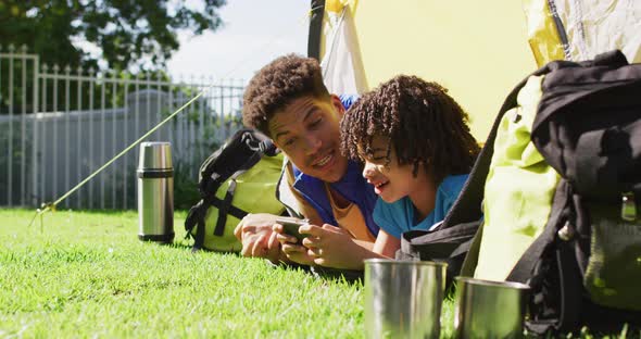 Happy biracial man and his son using smartphone in garden alt