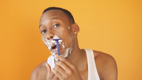 A Young African American Man Shaves His Beard on Camera on an Isolated Background alt