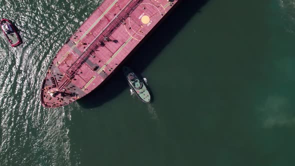 Top down view of Tug boats assisting big cargo ship. Large cargo ship enters the port escorted by tu alt