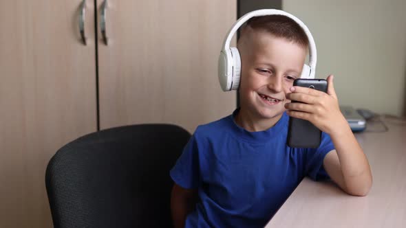 A schoolboy is communicating on wireless headphones with teacher while online education on smartphon