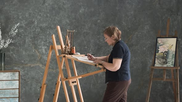 Elderly Woman Painting at Easel in Art Studio alt