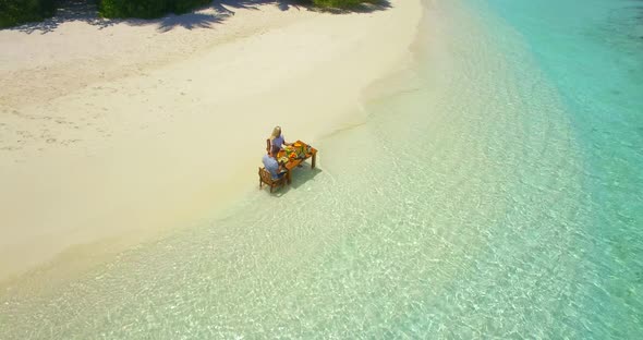 Aerial drone view of a man and woman eating breakfast on a tropical island beach. alt