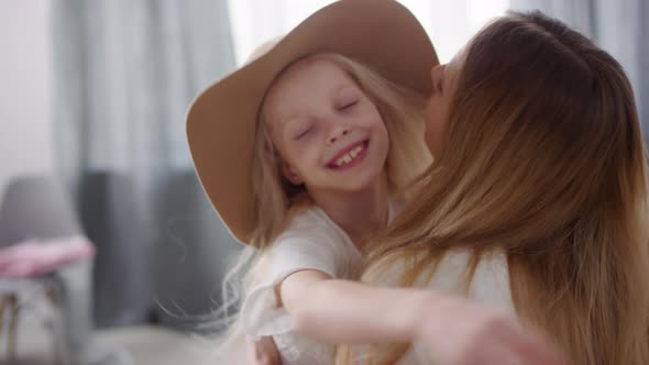 Adorable Little Girl in Wide Brim Hat Hugging Mother at Home alt