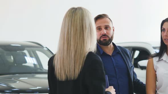 Professional Woman Salesman in Suit Holding Clipboard and Showcasing Car To Male and Female Client