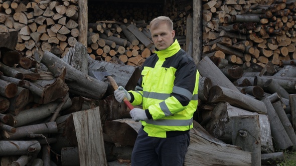 Lumberjack in Reflective Jacket. Man Woodcutter Hold Small Axe. Sawn Logs, Firewood Background alt