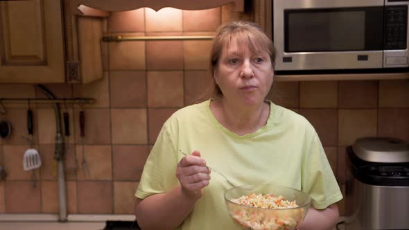 Eating disorder, hungry middle aged woman opens a refrigerator at night and eating unhealthy food. alt