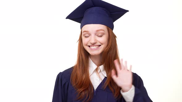 Happy Smiling Redhead Graduate Caucasian Girl in Blue Academic Dress Waving Her Hand alt