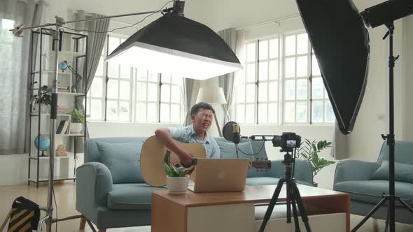 Asian Boy Playing Guitar And Sing A Song While Streaming. Professional Light Equipment alt