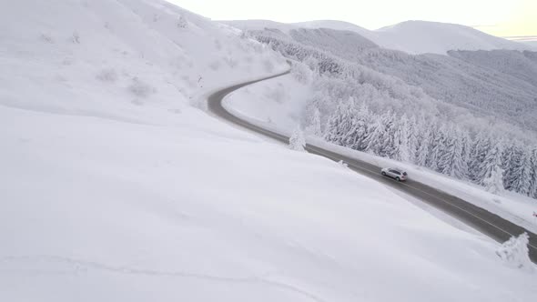 Drone Follows Silver SUV Speeding Uphill on Steep Mountain Road in Winter Conditions alt