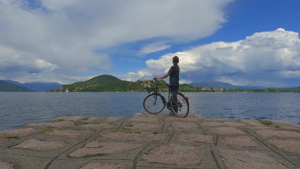 Back view of solitary woman holding bicycle on concrete jetty edge of Maggiore lake in Italy alt