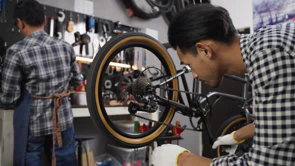 Young Asian man worker repairing bicycle wheel and gear in bicycle workshop