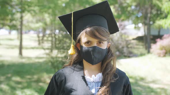 A Female Graduate Student in a Graduation Gown Removes a Medical Mask During the Coronavirus