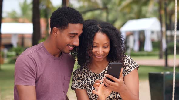 Carefree African Young Couple Watching at a Smartphone Smiling and Laughing alt