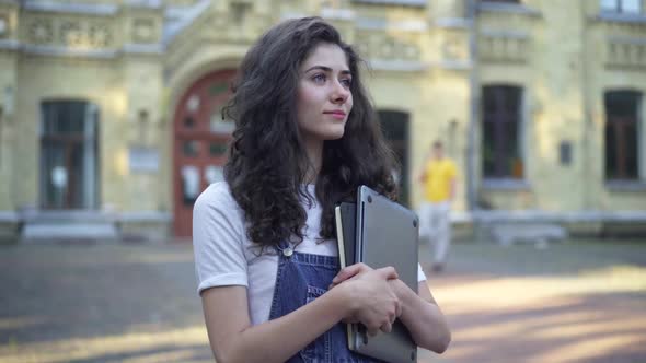 Happy Female Student Standing on Sunny University Yard Smiling Looking Away alt