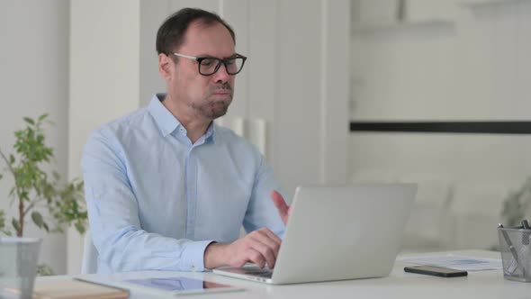 Middle Aged Man Coughing While Using Laptop in Office alt