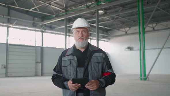 Handheld Adult Man Technical Engineer Walks on a Warehouse and Uses a Screen Tablet Perform a alt