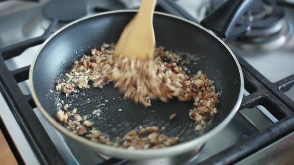 Woman stirring chopped nuts in pan on stovetop
