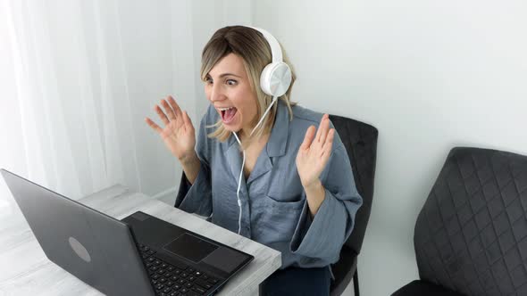 Amazed excited young blonde woman in headphones surprise looking at laptop computer with big eyes